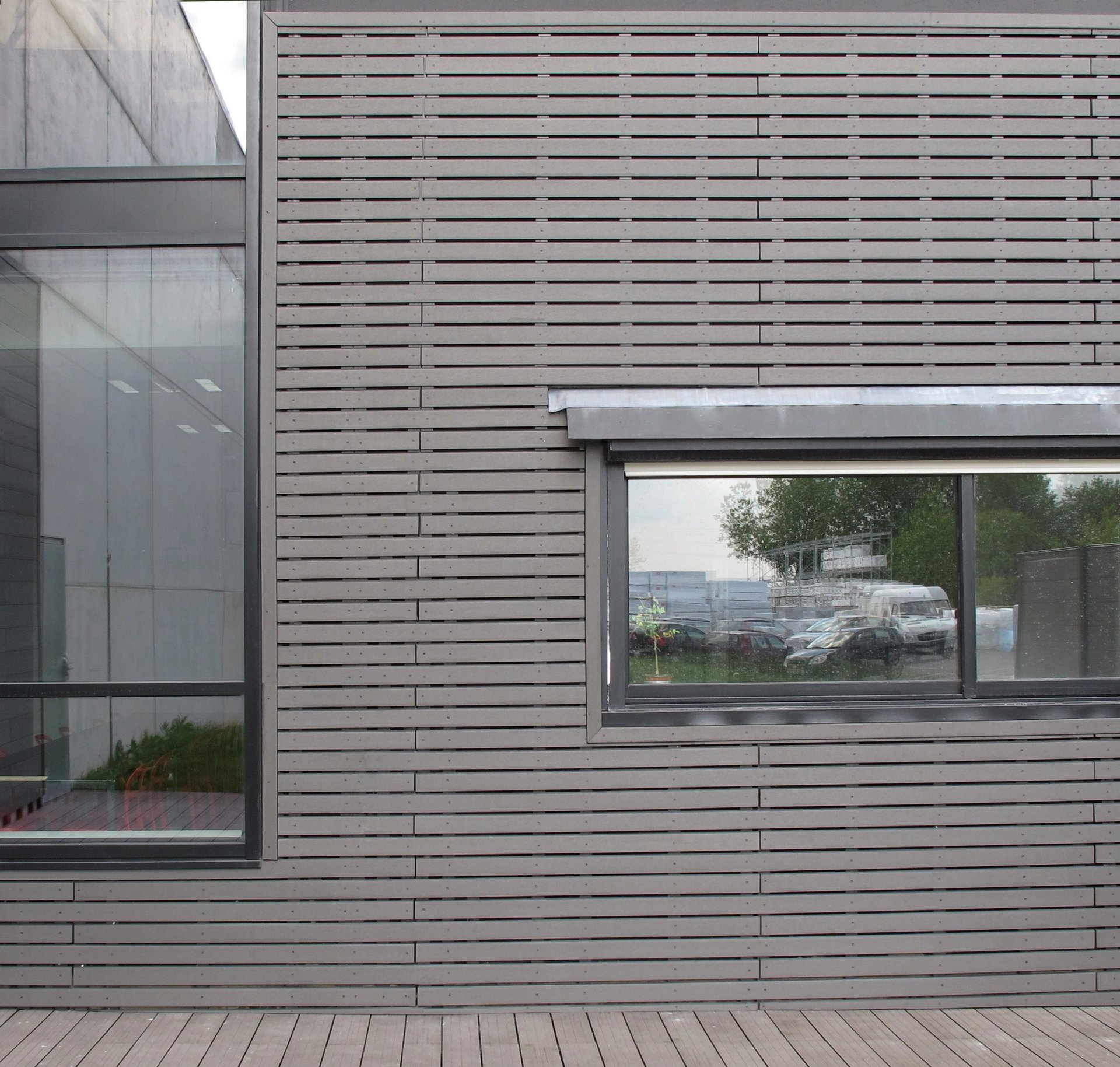 Façade en bardage ajouré ébène avec fenêtre vitrée et terrasse bois