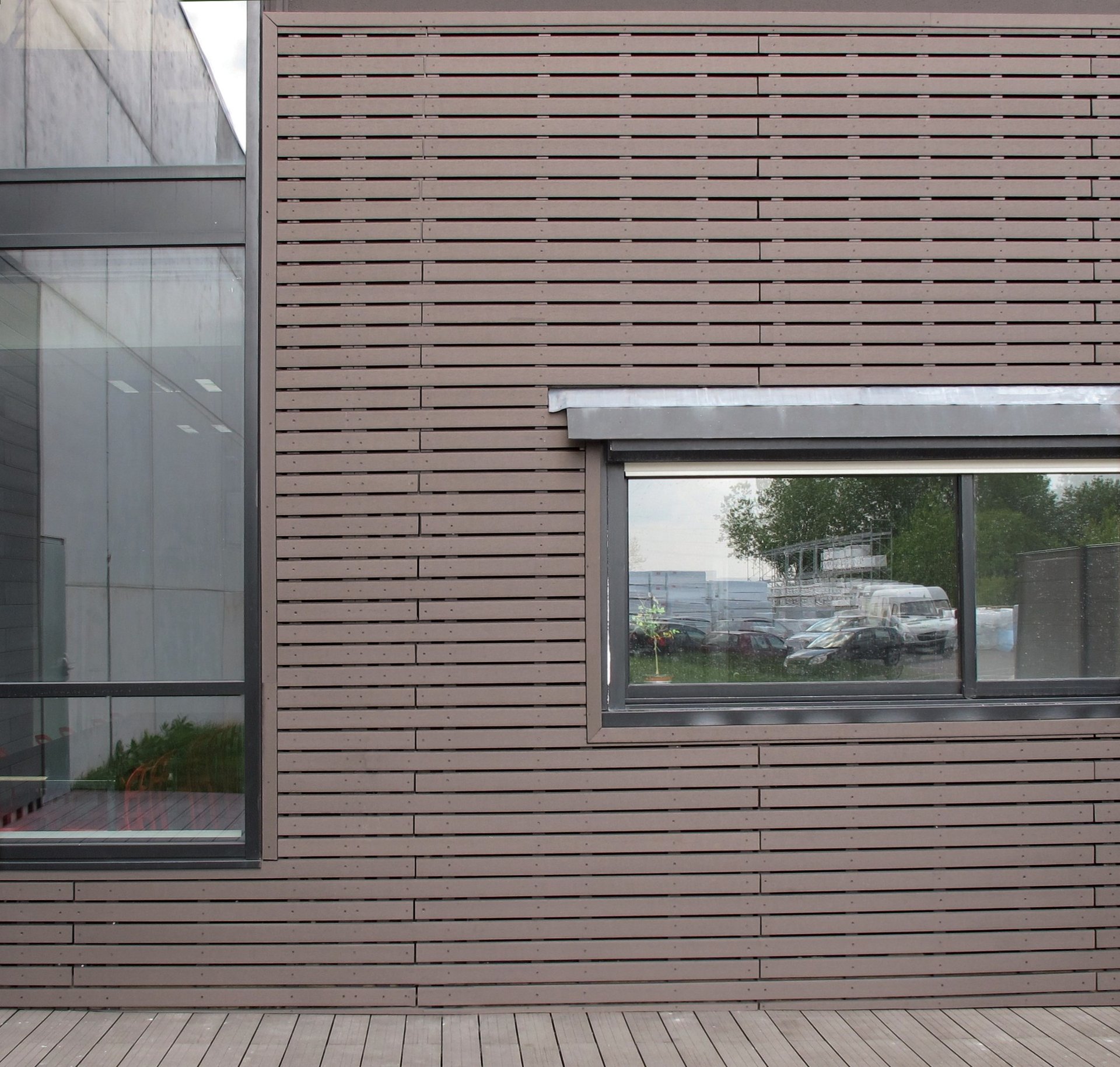 Façade en bardage ajouré chocolat avec fenêtre vitrée et terrasse bois