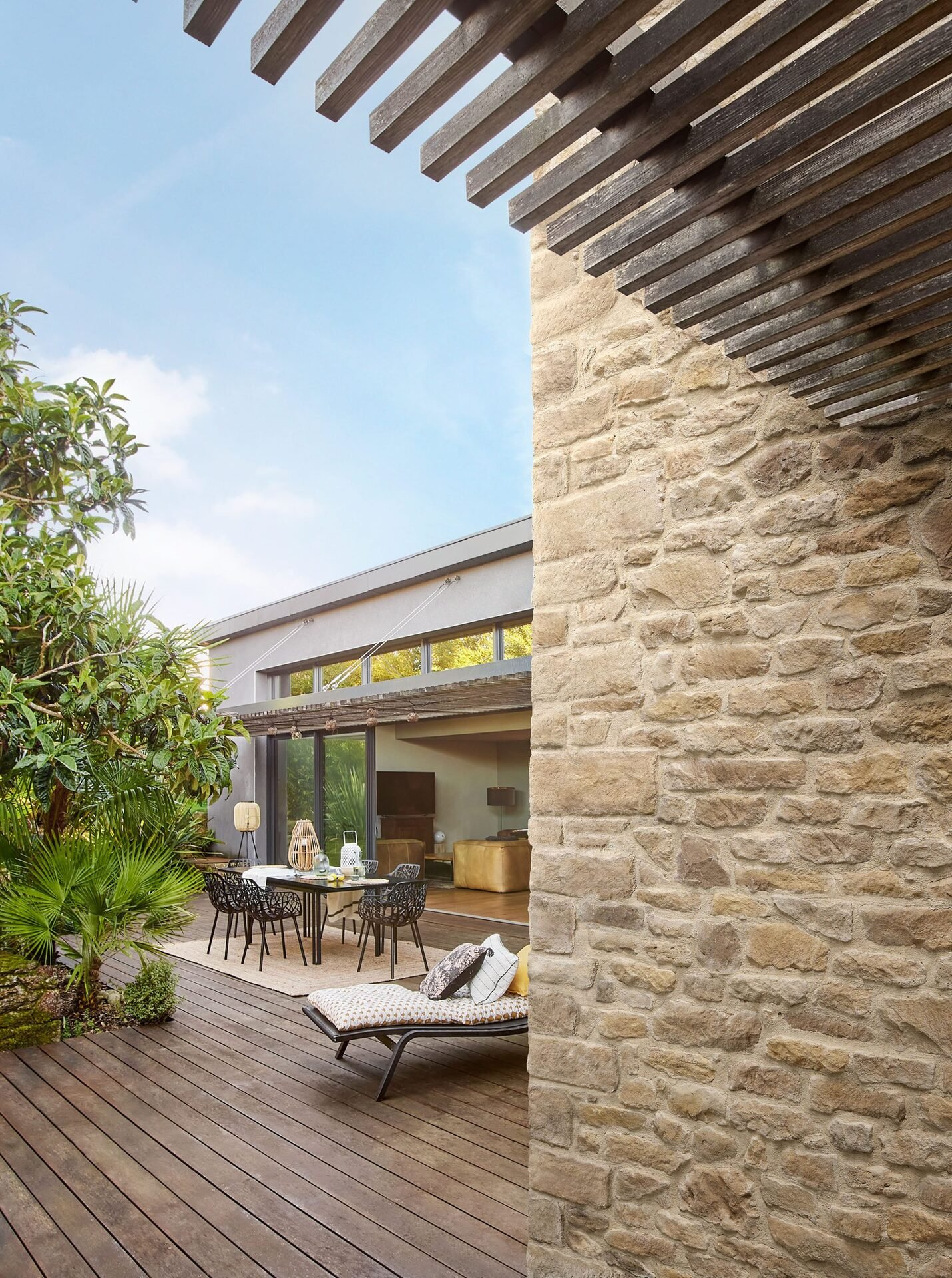 Façade extérieure en parement pierre Causse ton beige avec terrasse en bois, mobilier de jardin